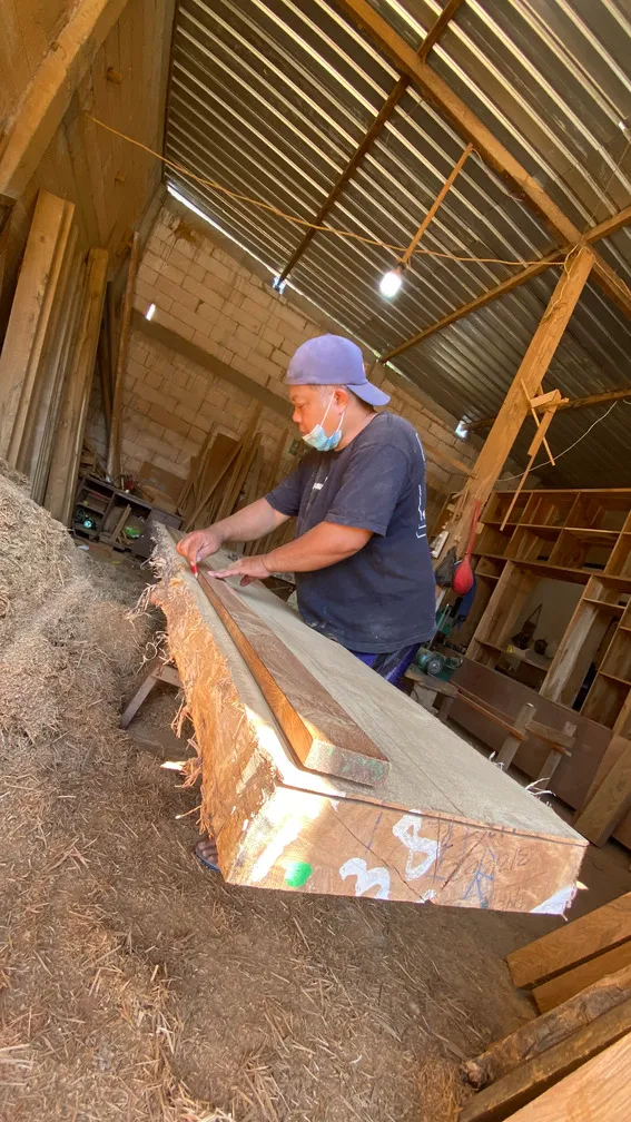 Pengrajin memeriksa papan kayu panjang di meja kerja